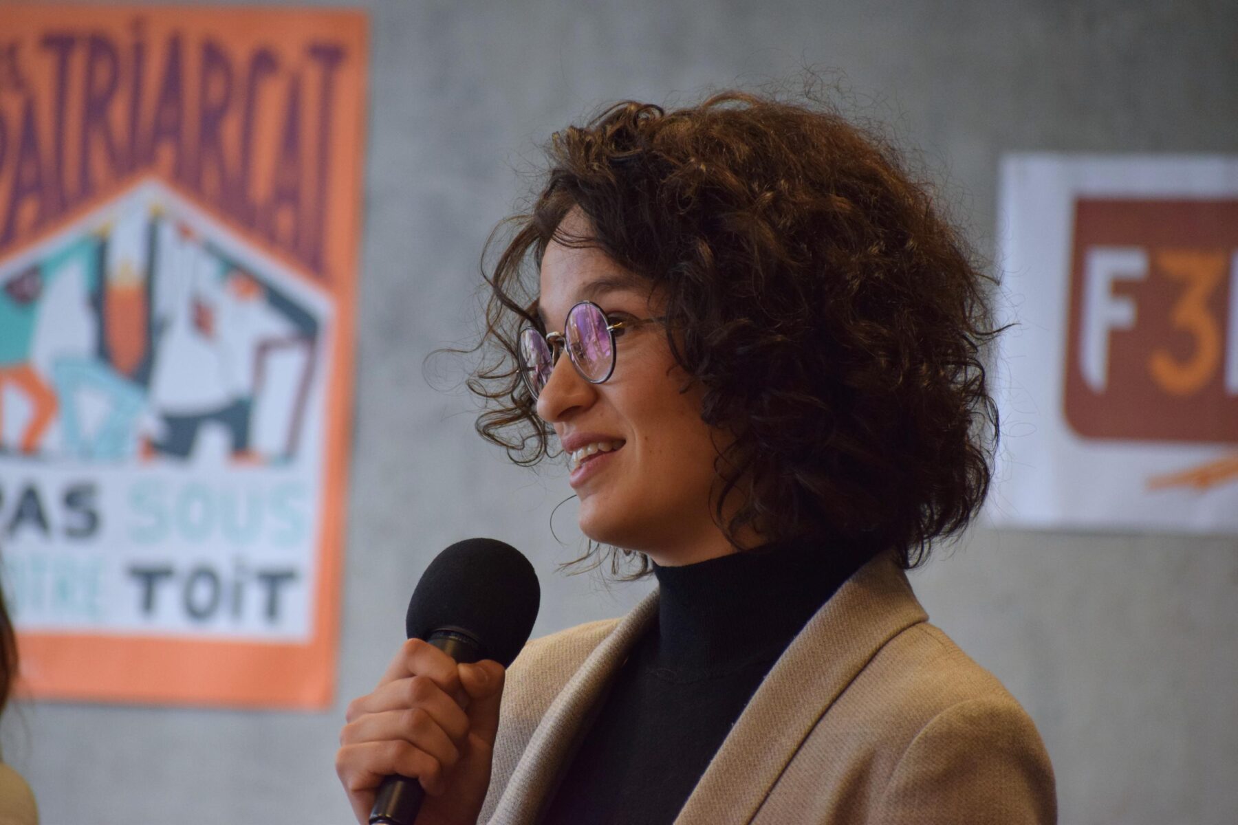 Portrait d'une femme avec des lunettes et cheveux bruns bouclés parlant au micro