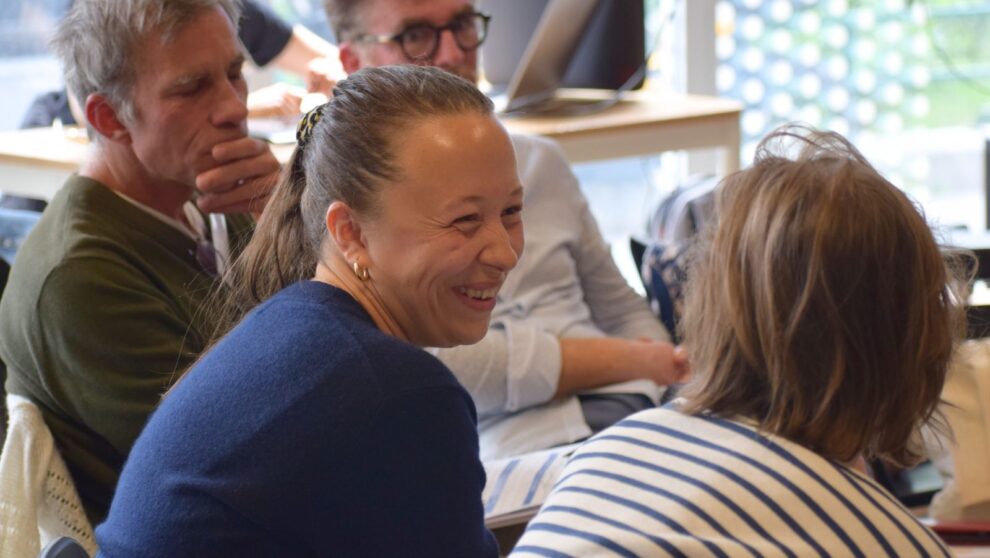 Une groupe d'adultes est assis, au premier plan deux femmes se regardent et rient