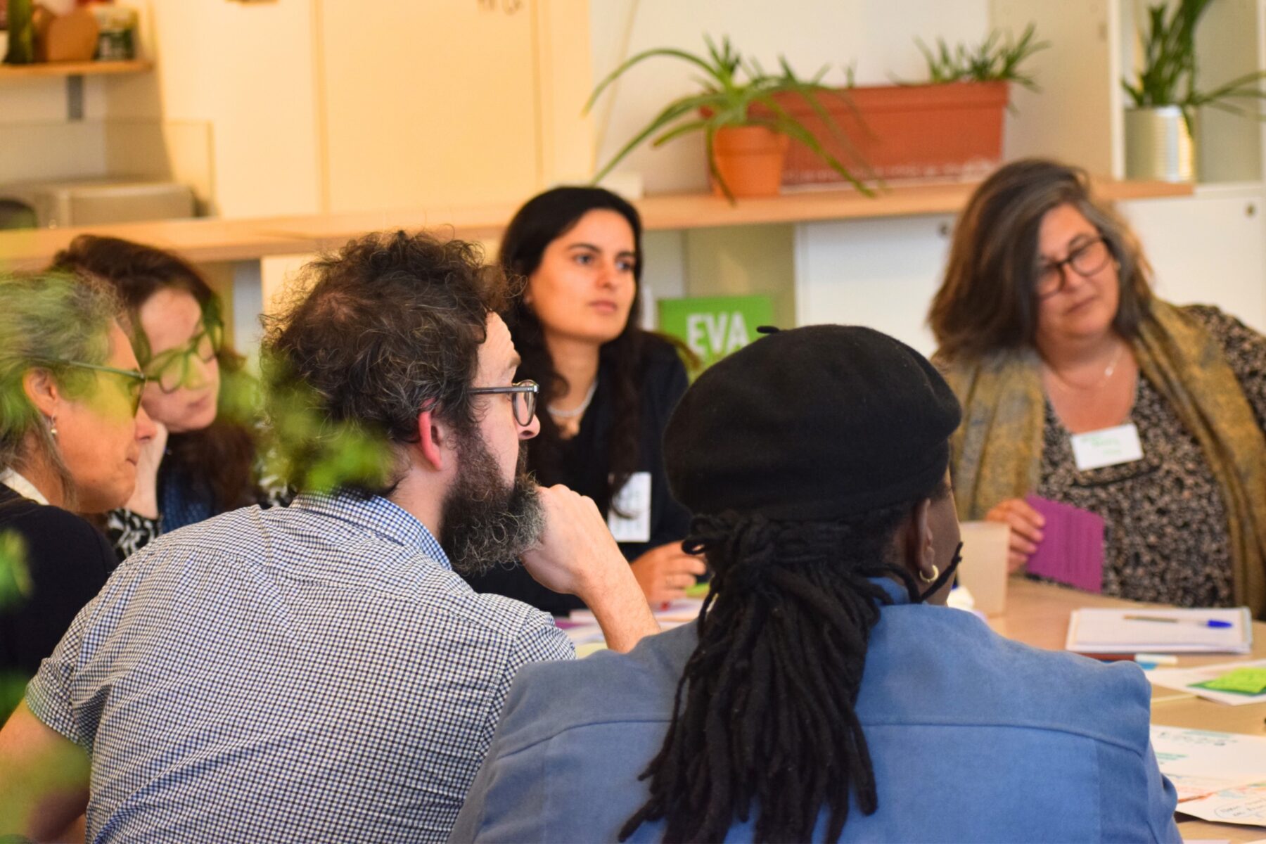 Un groupe d'adultes assis autour d'une table de travail, parle et échange entre elles et eux