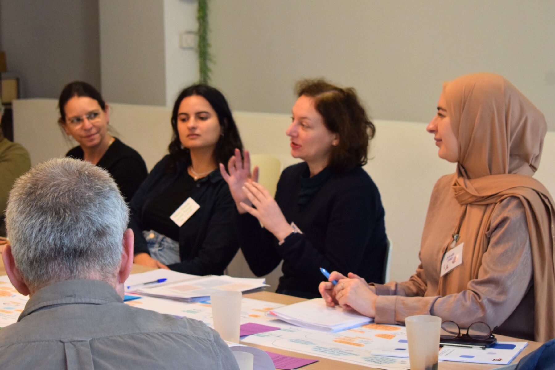 Un groupe d'adultes assis autour d'une table de travail écoute une adulte au centre, parler