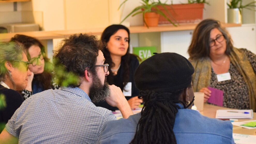 Un groupe d'adultes assis autour d'une table de travail, parle et échange entre elles et eux