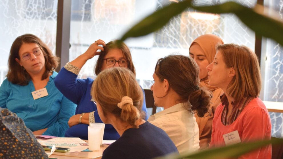Un groupe d'adultes assis autour d'une table de travail échange et discutent entre elles et eux