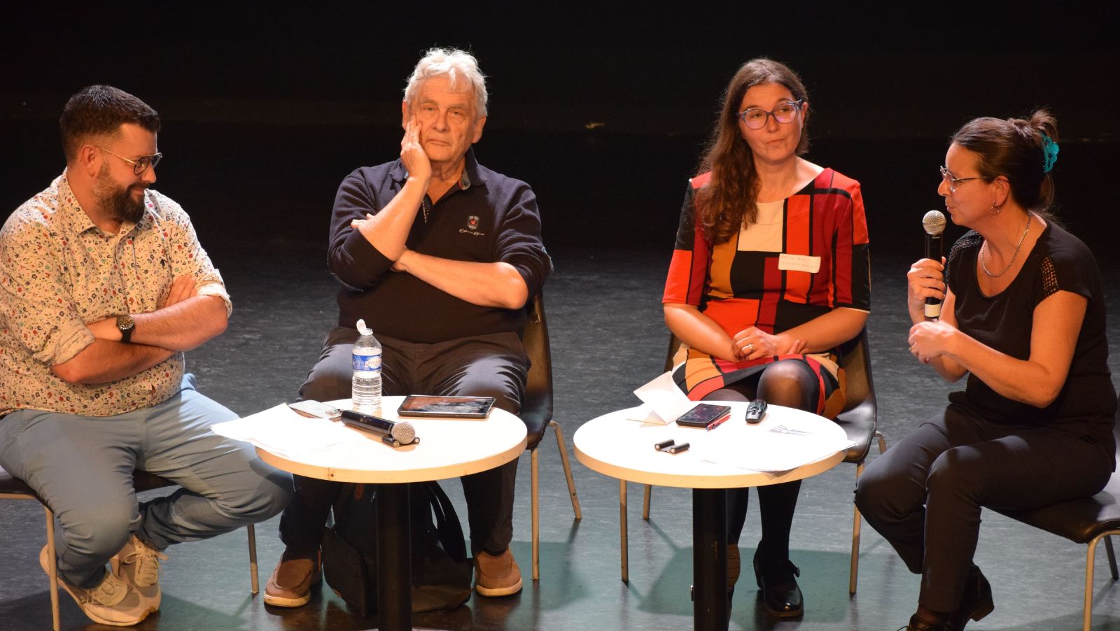 Quatre adultes assis-e-s en demi cercle sur une scène parle à une audience