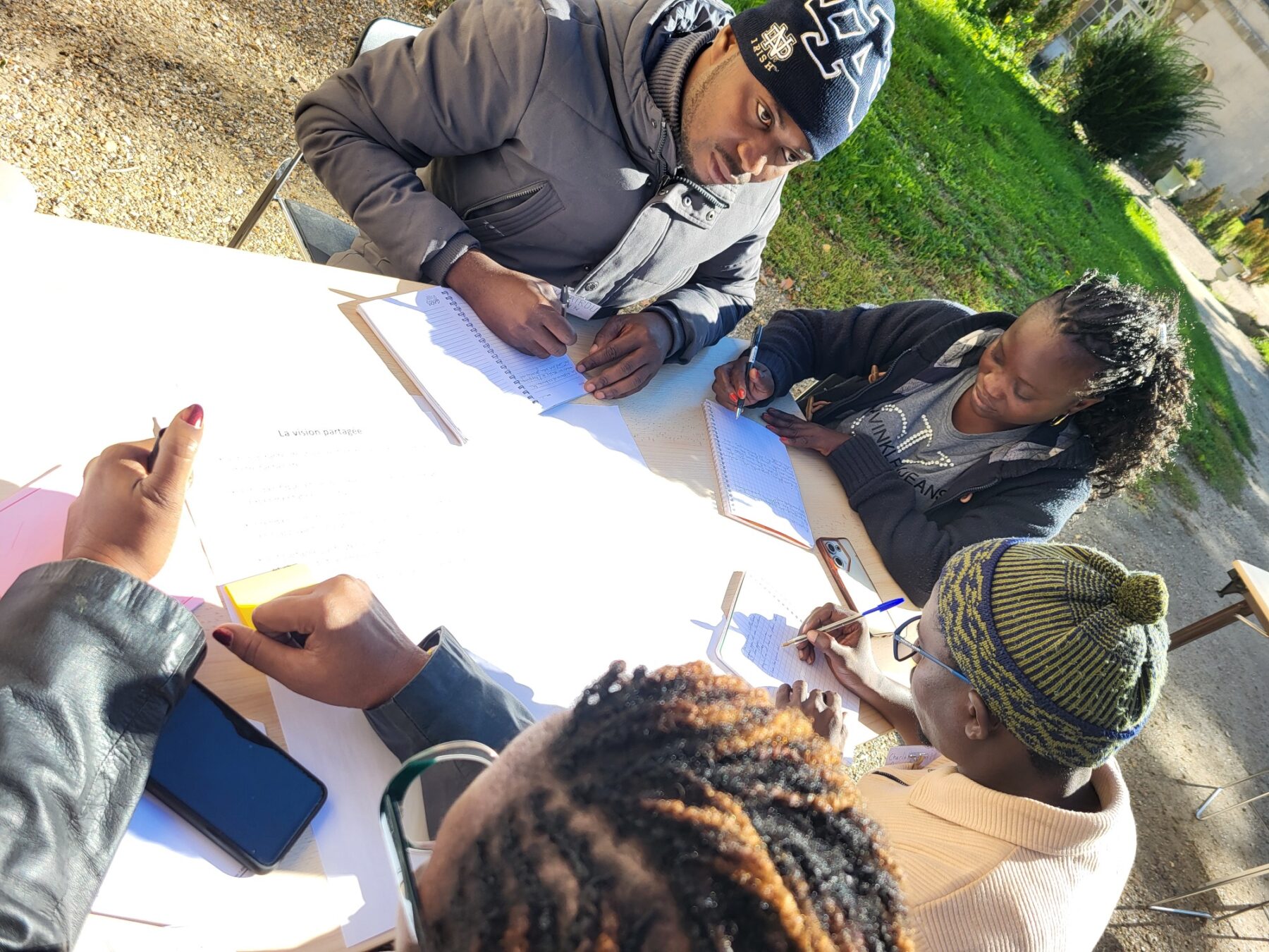 Un groupe d'adultes assis dehors, autour d'une table, travaillent ensemble