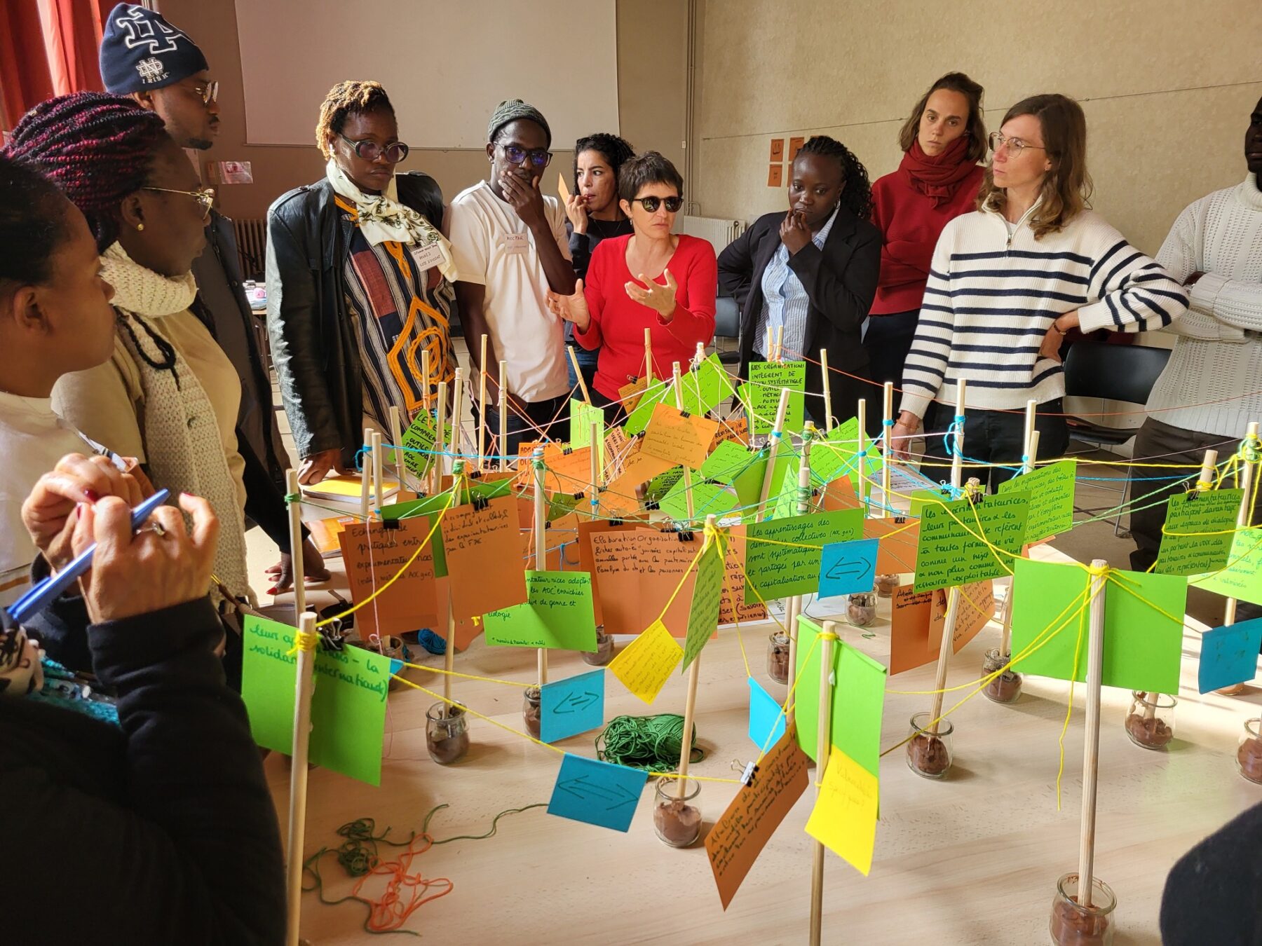 Un groupe d'adulte dans une pièce ensoleillé parle et échangent autour d'une table de travail sur laquelle sont disposées des post-it colorés