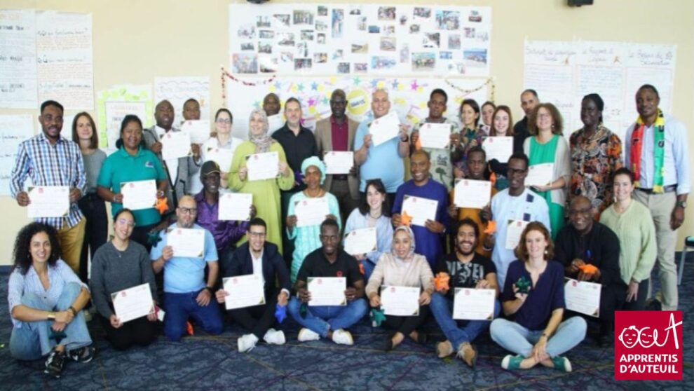 Un large groupe de jeunes adultes assis-e-s par terre sourit à la caméra