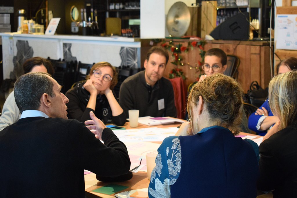 Un groupe d'adultes assis-e-s autour d'une table, discute